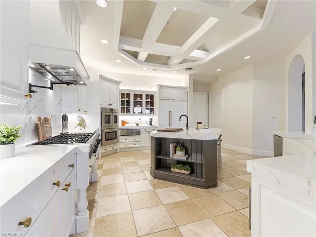 Kitchen with coffered ceiling, open shelves, recessed lighting, custom exhaust hood, and light stone countertops
