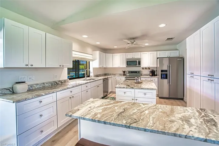 Kitchen with stainless steel appliances, a sink, white cabinetry, and light stone counters