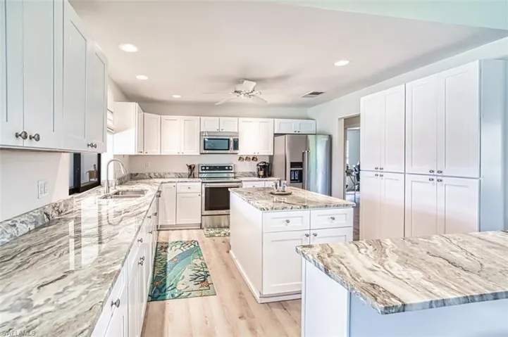 Kitchen featuring stainless steel appliances, a sink, light wood-type flooring, a center island, and light stone countertops