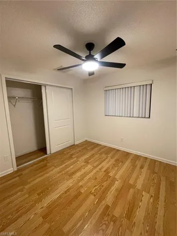 Unfurnished bedroom with a textured ceiling, a closet, light wood-style floors, and a ceiling fan