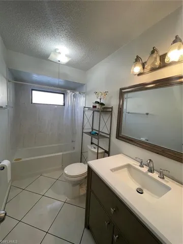 Bathroom with a textured ceiling, vanity, shower / bath combo, and tile patterned flooring