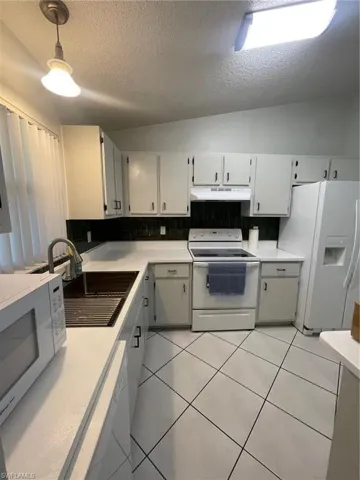 Kitchen with a textured ceiling, refrigerator, range, light tile patterned floors, and tasteful backsplash