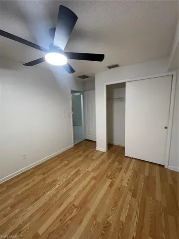 Unfurnished bedroom featuring a textured ceiling, light wood-style flooring, a ceiling fan, and a closet