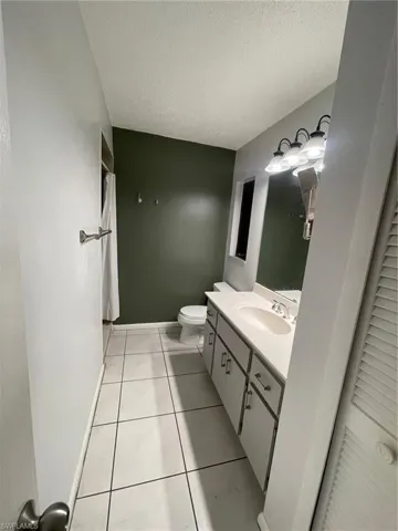 Full bath featuring a textured ceiling, vanity, tile patterned floors, and curtained shower