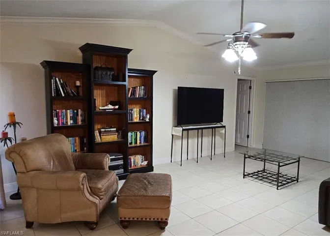 Living area with vaulted ceiling, ornamental molding, light tile patterned floors, and ceiling fan