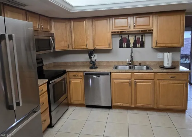 Kitchen featuring appliances with stainless steel finishes, light tile patterned floors, light countertops, and brown cabinetry