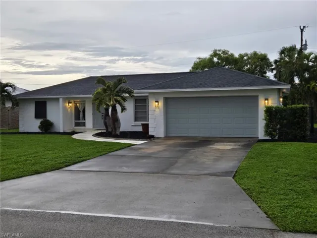 Ranch-style home featuring a shingled roof, a front yard, driveway, and a garage