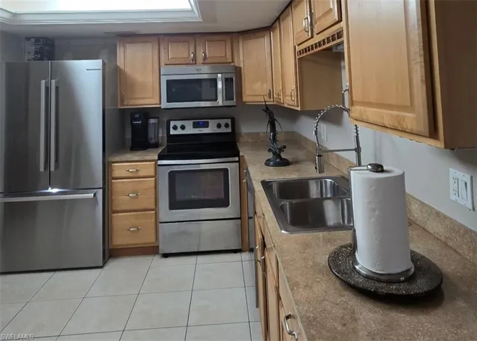 Kitchen with appliances with stainless steel finishes, light tile patterned flooring, light countertops, and brown cabinets