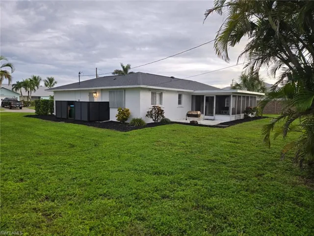 Rear view of property featuring a sunroom, a lawn, and stucco siding