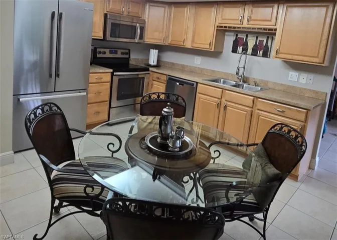 Kitchen with light tile patterned flooring, appliances with stainless steel finishes, light countertops, and brown cabinetry