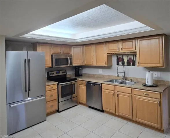Kitchen with stainless steel appliances, light tile patterned floors, light countertops, brown cabinets, and a textured ceiling