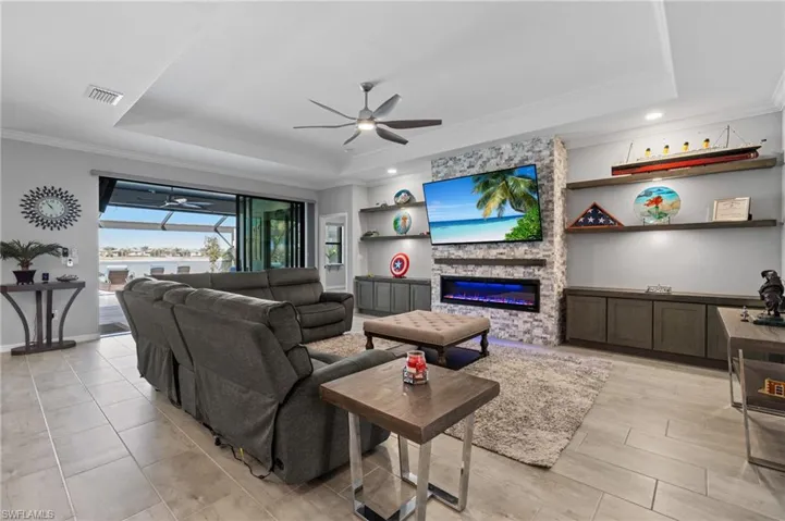 Living room with a fireplace, a ceiling fan, ornamental molding, and a raised ceiling