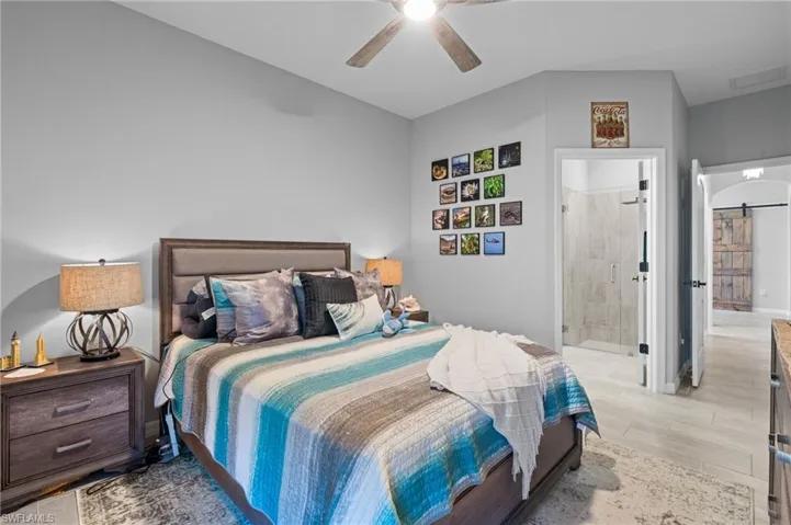 Bedroom featuring ensuite bathroom, visible vents, light wood finished floors, ceiling fan, and a barn door