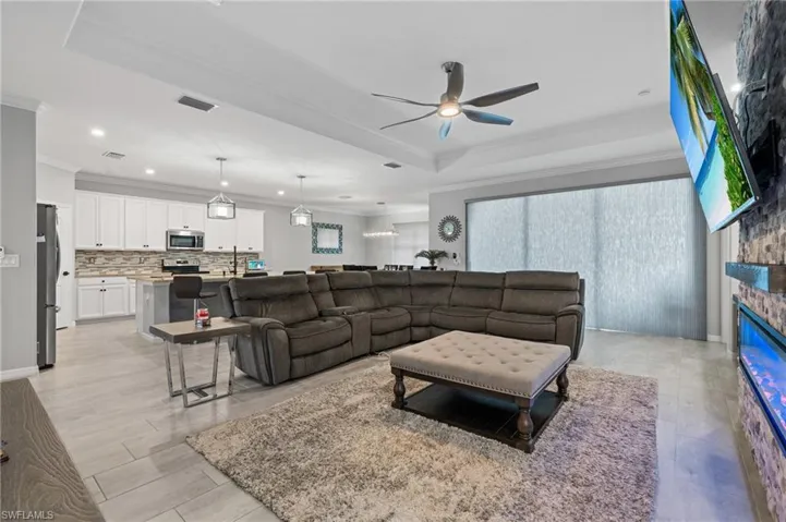 Living area featuring a raised ceiling, a fireplace, visible vents, ceiling fan, and ornamental molding