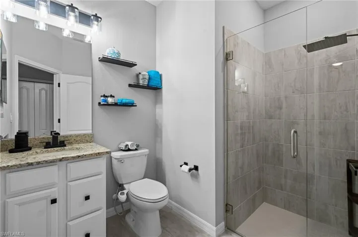 Full bath featuring a shower stall, baseboards, toilet, and vanity