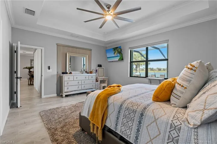 Bedroom featuring baseboards, a raised ceiling, light wood finished floors, visible vents, and a ceiling fan