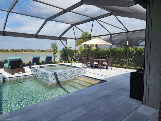View of swimming pool with a pool with connected hot tub, a water view, a lanai, and a patio