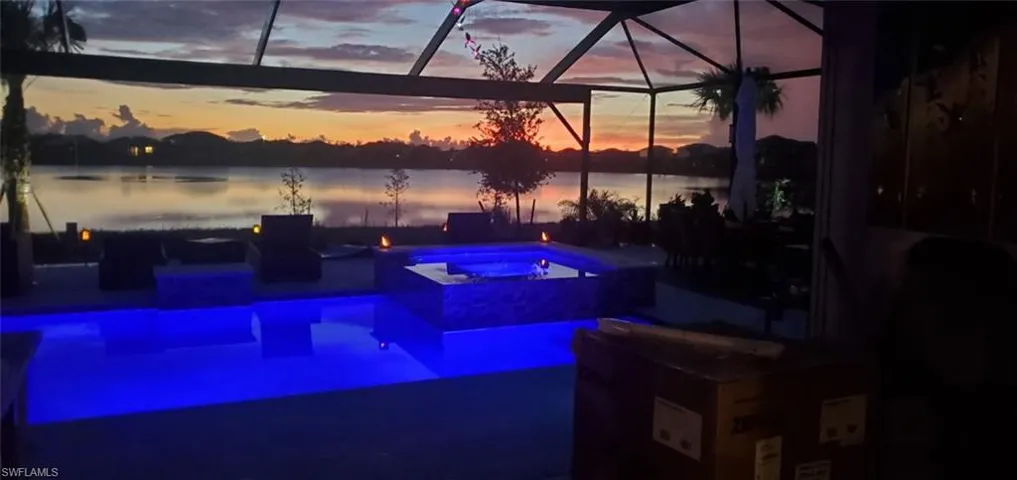 View of pool with glass enclosure, a pool with connected hot tub, a water view, and a patio