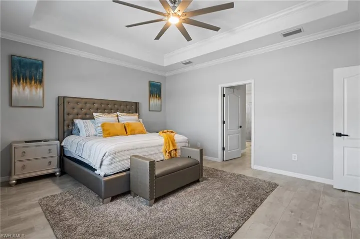 Bedroom with a tray ceiling, baseboards, visible vents, and ornamental molding