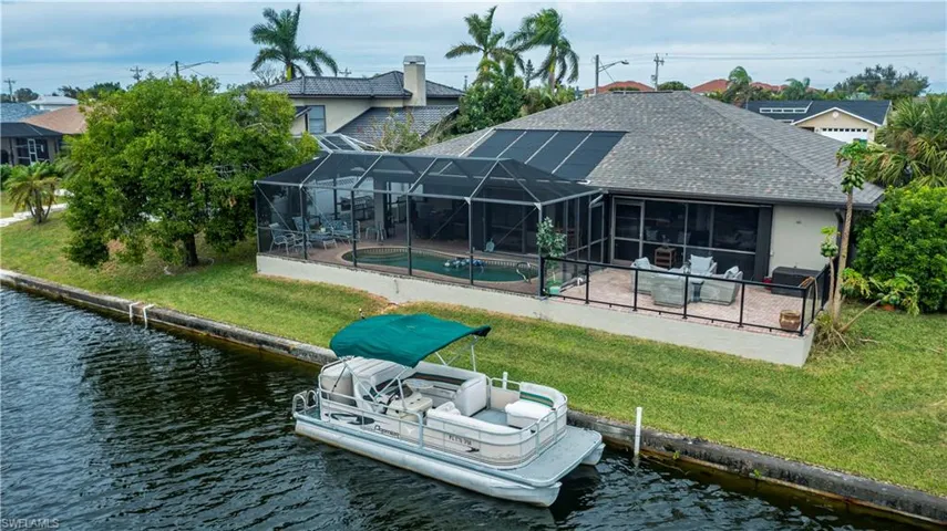 Rear view of house with a water view, a patio area, a lanai, and a lawn