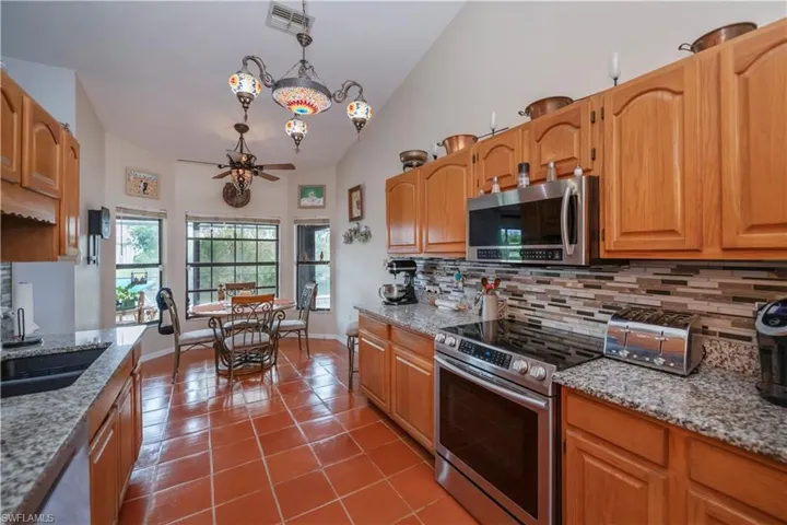 Kitchen with stainless steel appliances, tile patterned floors, light stone counters, high vaulted ceiling, and decorative backsplash