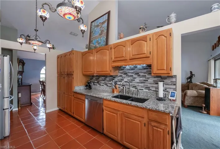 Kitchen with tasteful backsplash, sink, stainless steel appliances, lofted ceiling, and decorative light fixtures