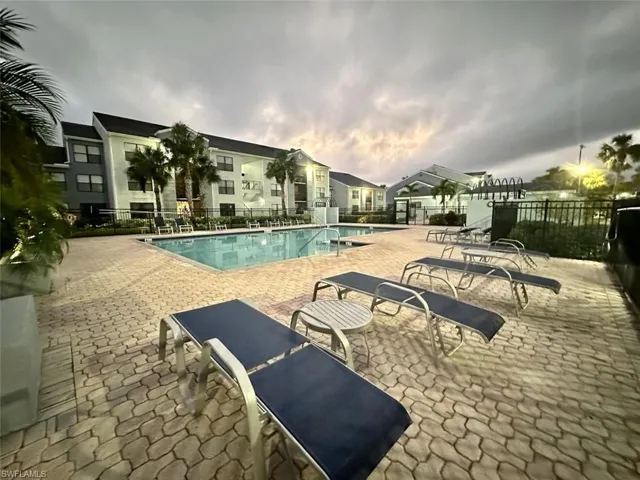 Paved pool deck featuring a swimming pool, multiple lounge chairs, and perimeter fencing