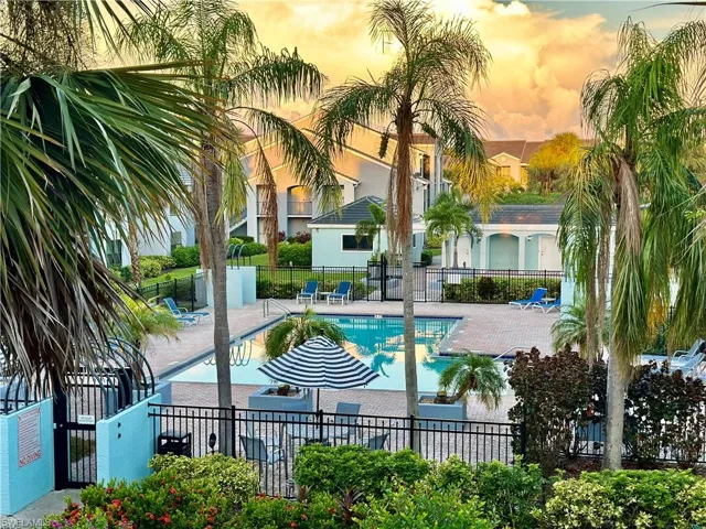 Community swimming pool with a surrounding paver deck, black wrought iron fencing, and lush tropical landscaping