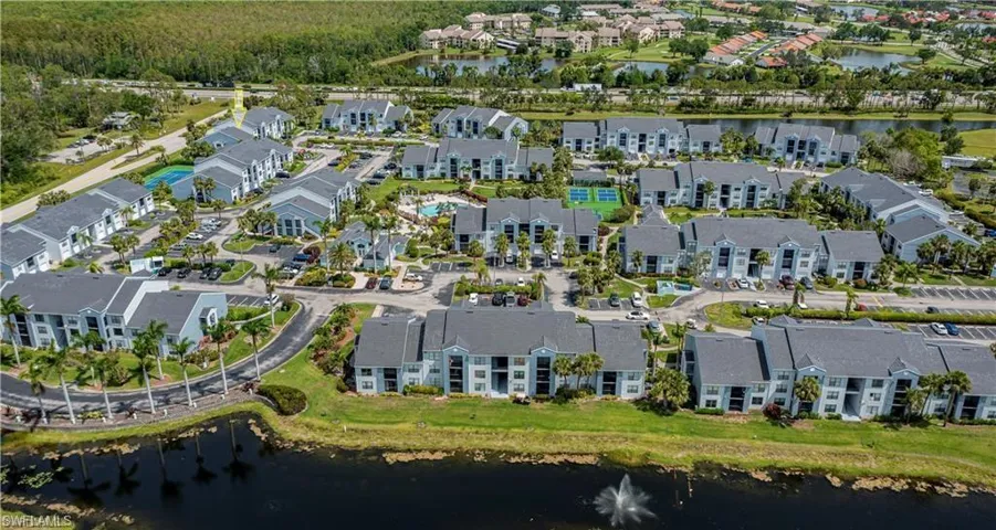 Aerial perspective of a multi-building community featuring numerous residences, a central swimming pool, tennis courts, and abundant mature landscaping