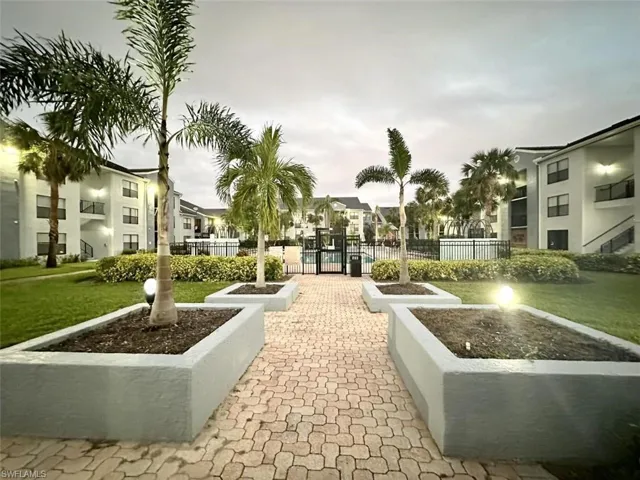 Paver pathway featuring integrated planters with palm trees, manicured lawns, and surrounding buildings with multiple levels