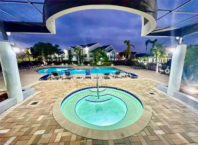 Illuminated spa and pool area featuring extensive paver decking