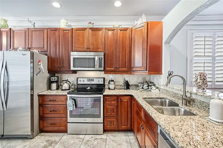 Kitchen with sink, crown molding, light tile floors, and appliances with stainless steel finishes
