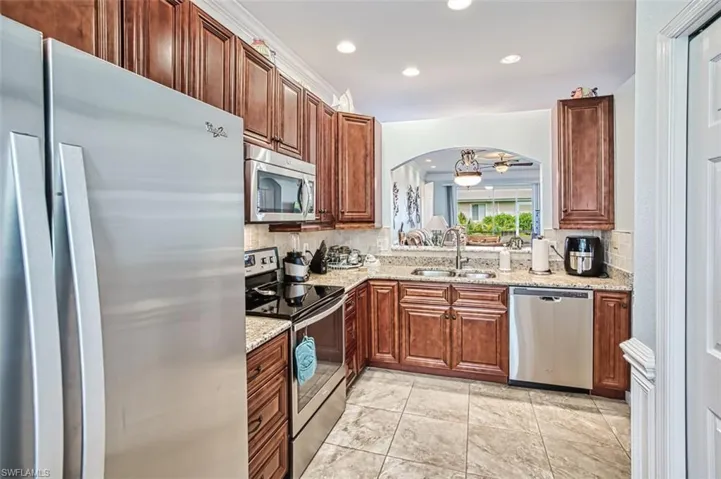 Kitchen featuring light stone counters, light tile flooring, backsplash, appliances with stainless steel finishes, and sink
