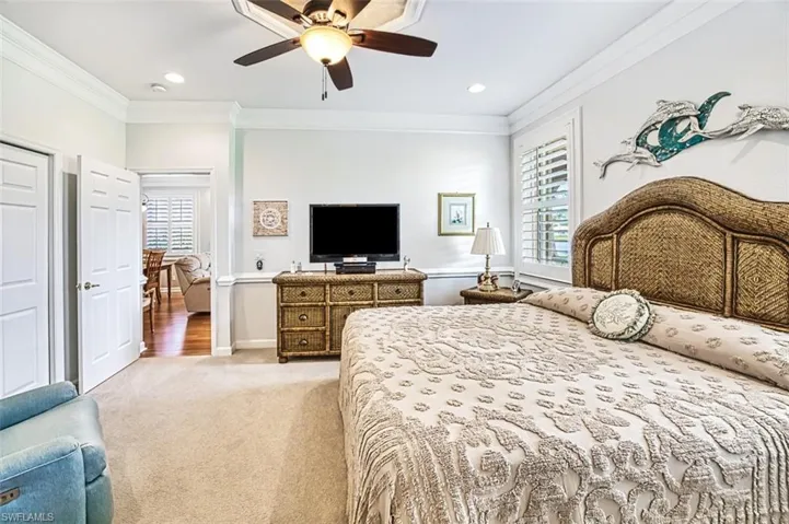 Carpeted bedroom featuring ceiling fan, multiple windows, and ornamental molding