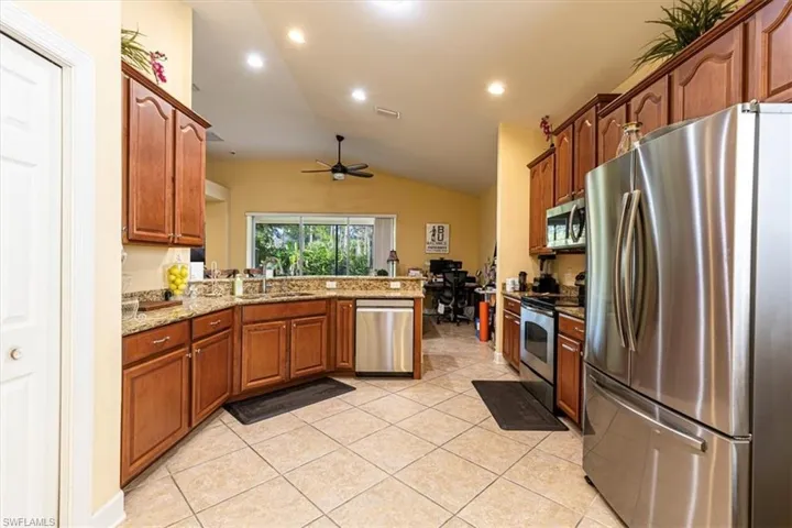 Kitchen with appliances with stainless steel finishes, light stone counters, vaulted ceiling, a peninsula, and brown cabinets
