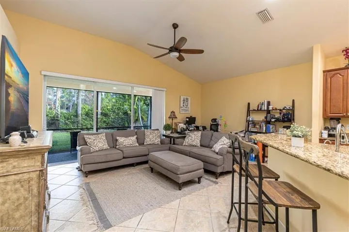 Living room with lofted ceiling, light tile patterned floors, and a ceiling fan