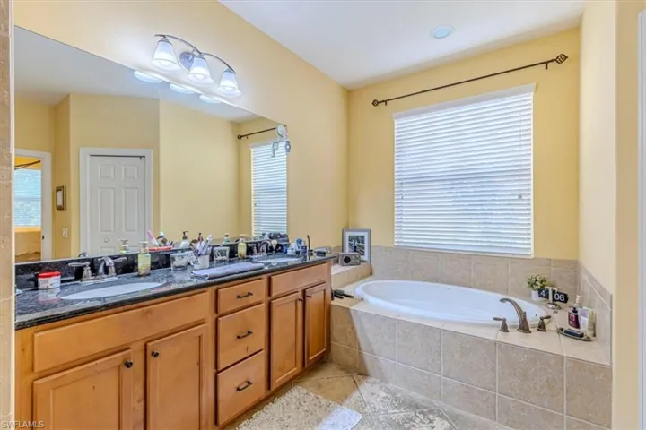 Full bath with double vanity, a garden tub, and light tile patterned floors