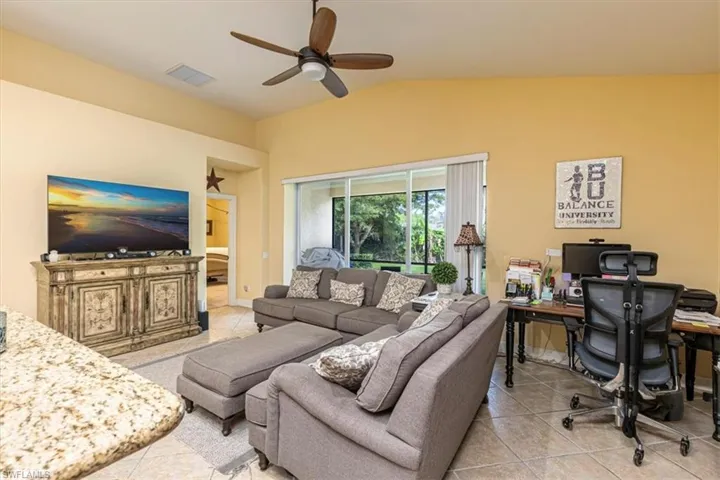 Living area featuring a desk, lofted ceiling, light tile patterned floors, and a ceiling fan