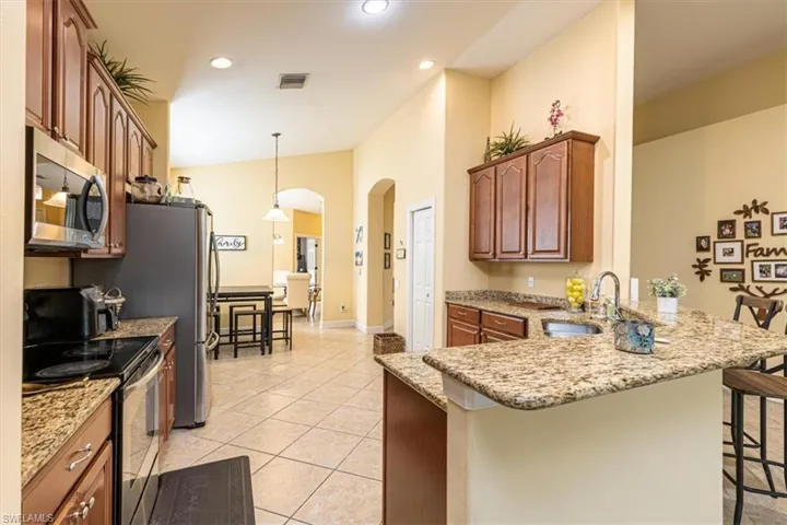 Kitchen featuring appliances with stainless steel finishes, light stone counters, arched walkways, pendant lighting, and recessed lighting