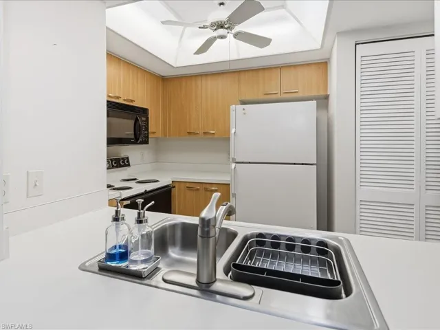 Kitchen featuring light wood-finish cabinetry, white countertops, built-in microwave, and ceiling fan with light fixture