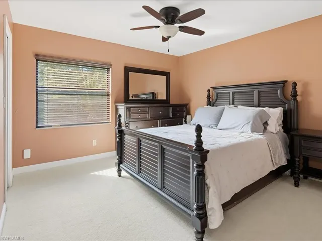 Master bedroom featuring warm peachy-toned walls, a ceiling fan with integrated lighting, large window with horizontal blinds providing natural light, wood-finish flooring, and dark wood dresser with mirror