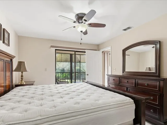 Sliding glass doors opening to a screened enclosure, ceiling fan with integrated lighting, and a wood-finish dresser with an arched mirror