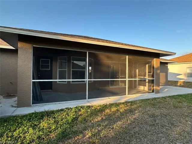 Rear view of property with stucco siding, a sunroom, and a lawn