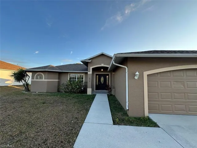 Ranch-style home with stucco siding, a garage, a front yard, and roof with shingles
