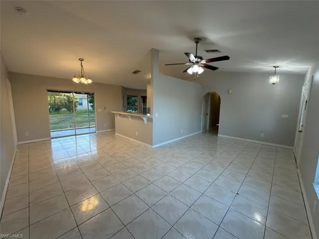 Spare room with a chandelier, vaulted ceiling, light tile patterned flooring, arched walkways, and a ceiling fan