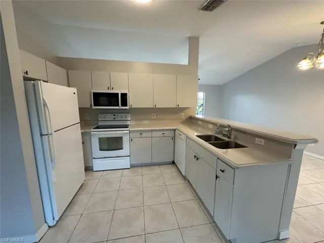 Kitchen with white appliances, light countertops, a chandelier, a peninsula, and decorative light fixtures
