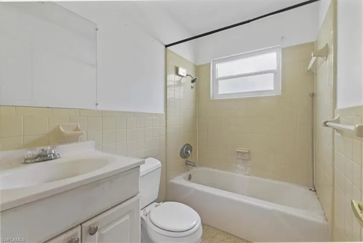 Full bath featuring tile walls, vanity, shower / tub combination, and wainscoting