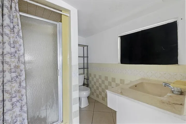Full bathroom featuring a shower stall, tile patterned floors, tile walls, a wainscoted wall, and vanity