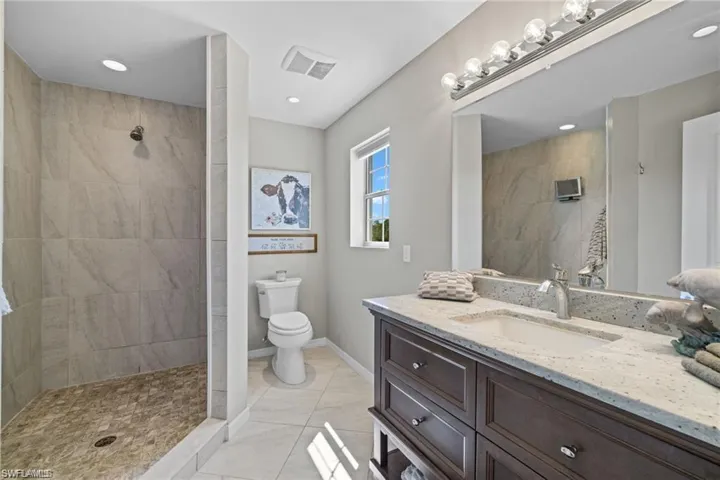 Bathroom with toilet, vanity, a tile shower, and tile patterned floors