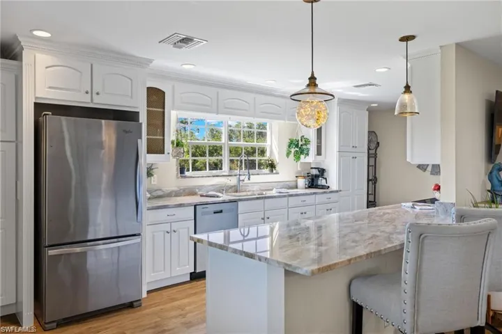 Kitchen featuring white cabinets, hanging light fixtures, a kitchen breakfast bar, light hardwood / wood-style floors, and stainless steel appliances